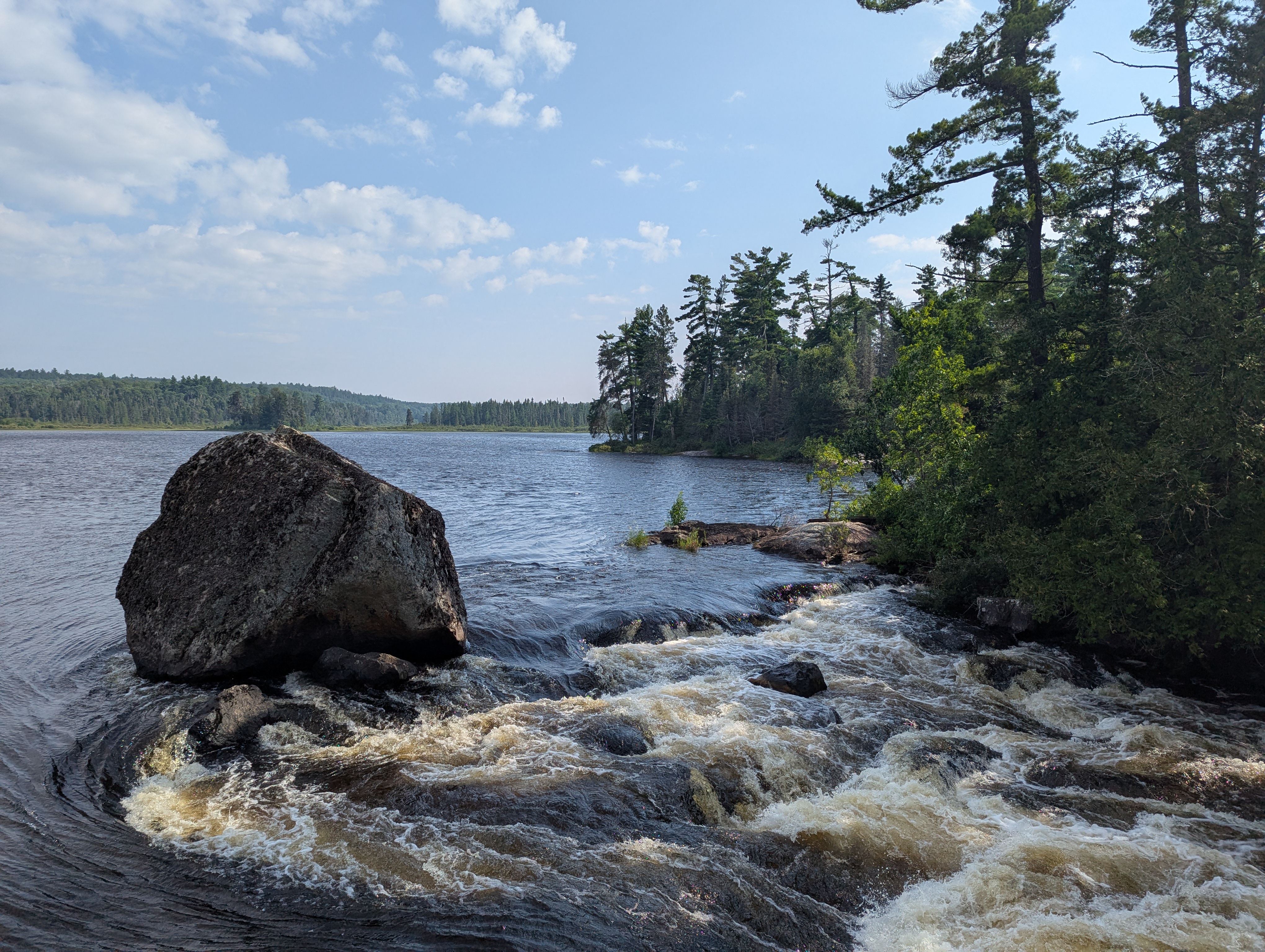 A large boulder at the top of a waterfall with water rushing past on both sides.