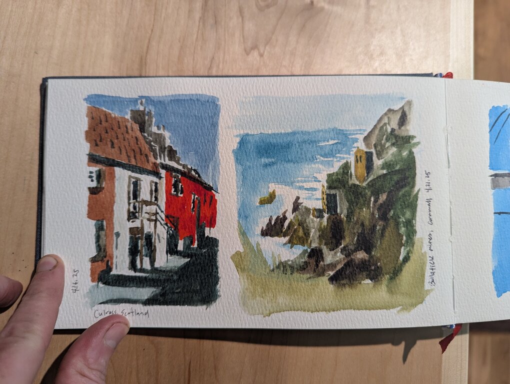 Two small landscape paintings. The first is a city street with white and bright orange buildings. The second is a seascape with two buildings perched on the rockface heading down to the water.
