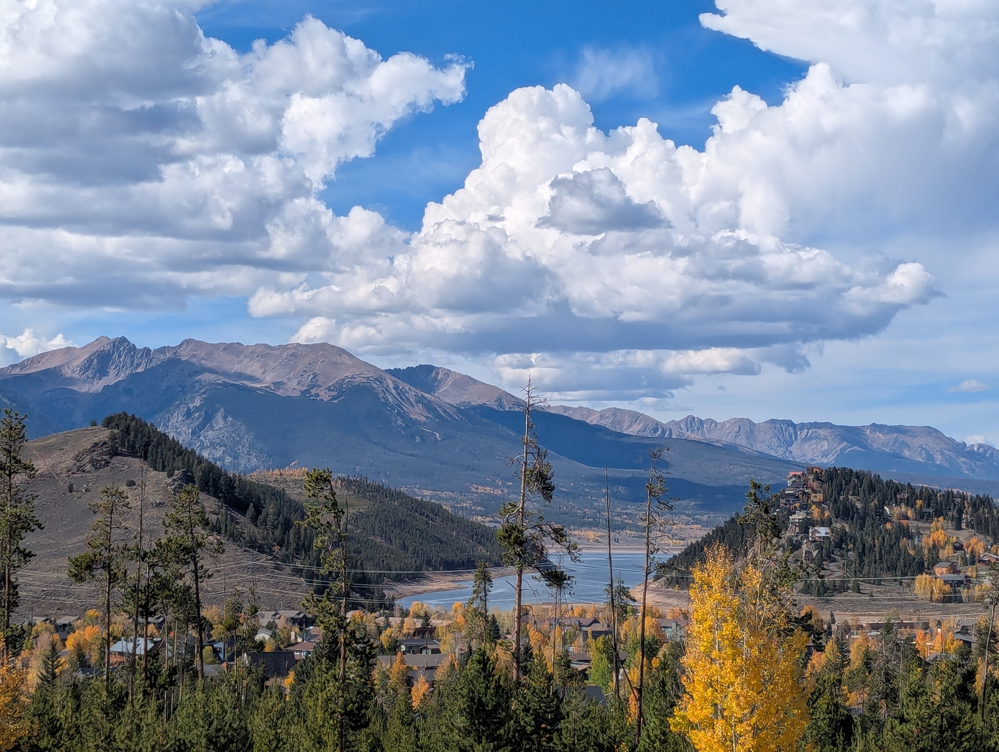 A large mountain cascades down to a low mountain lake. Houses can be seen below the trees in the foreground.