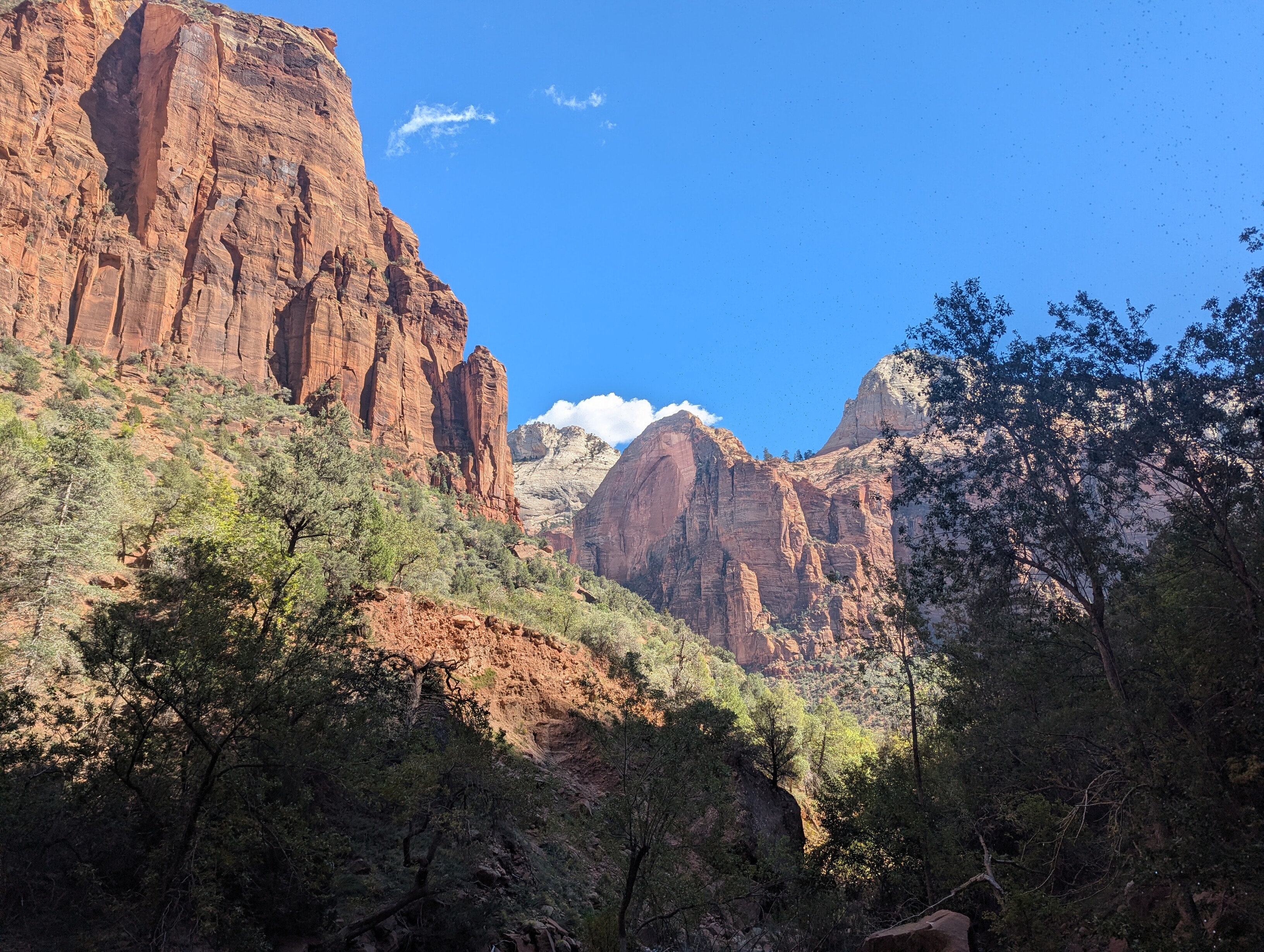 The viewer is in the low part of the canyon looking up. Two large red rock cliffs frame a taller, white cliff in the distance.