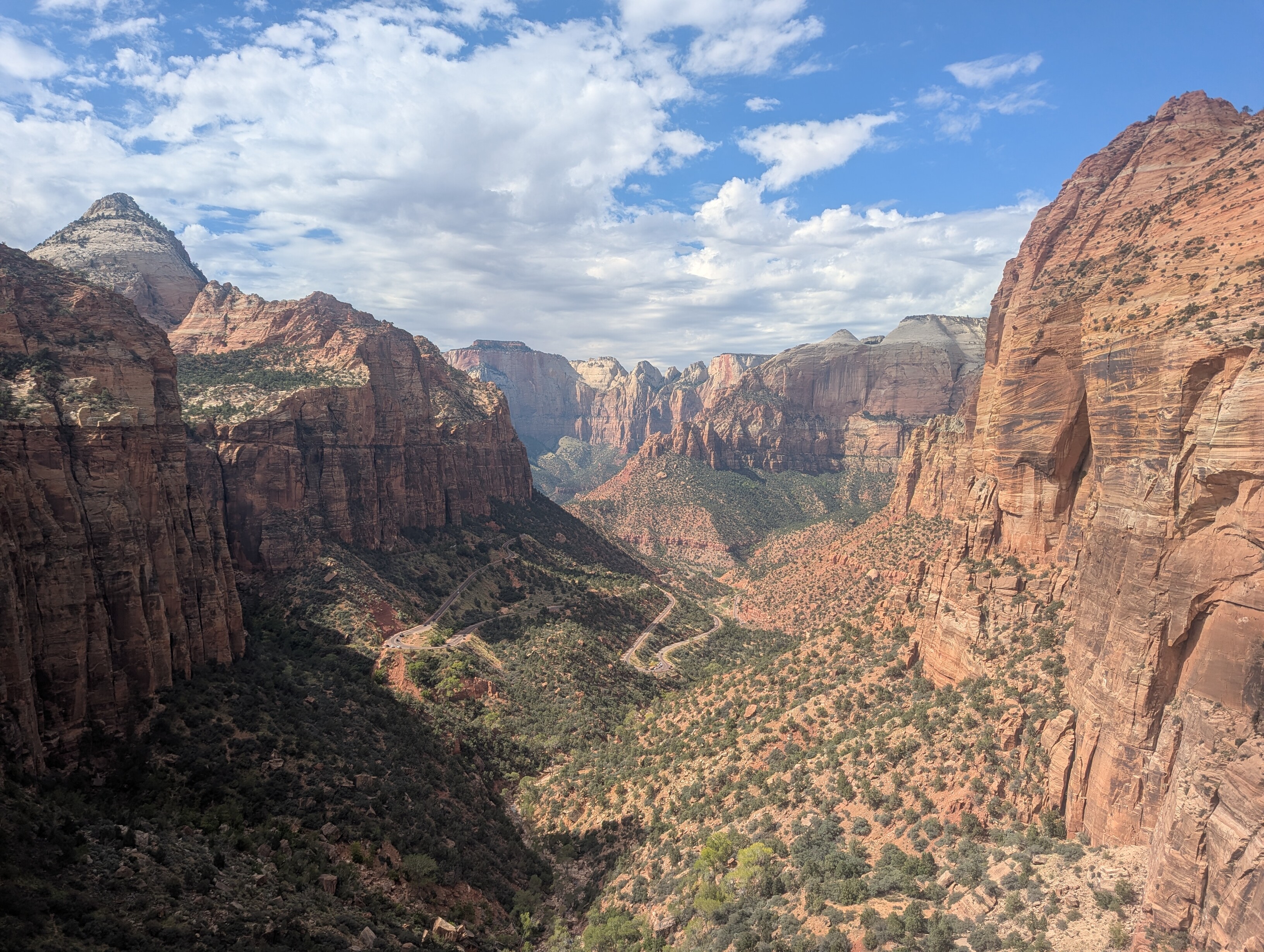 A wide view of the east end of Zion Canyon. The canyon walls converge in the distance. A long, switchbacked road is visible on the floor of the canyon.